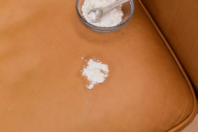 Bột ngô đổ lên vết dầu mỡ để loại bỏ khỏi chúng trên chiếc ghế sofa bọc da màu nâu