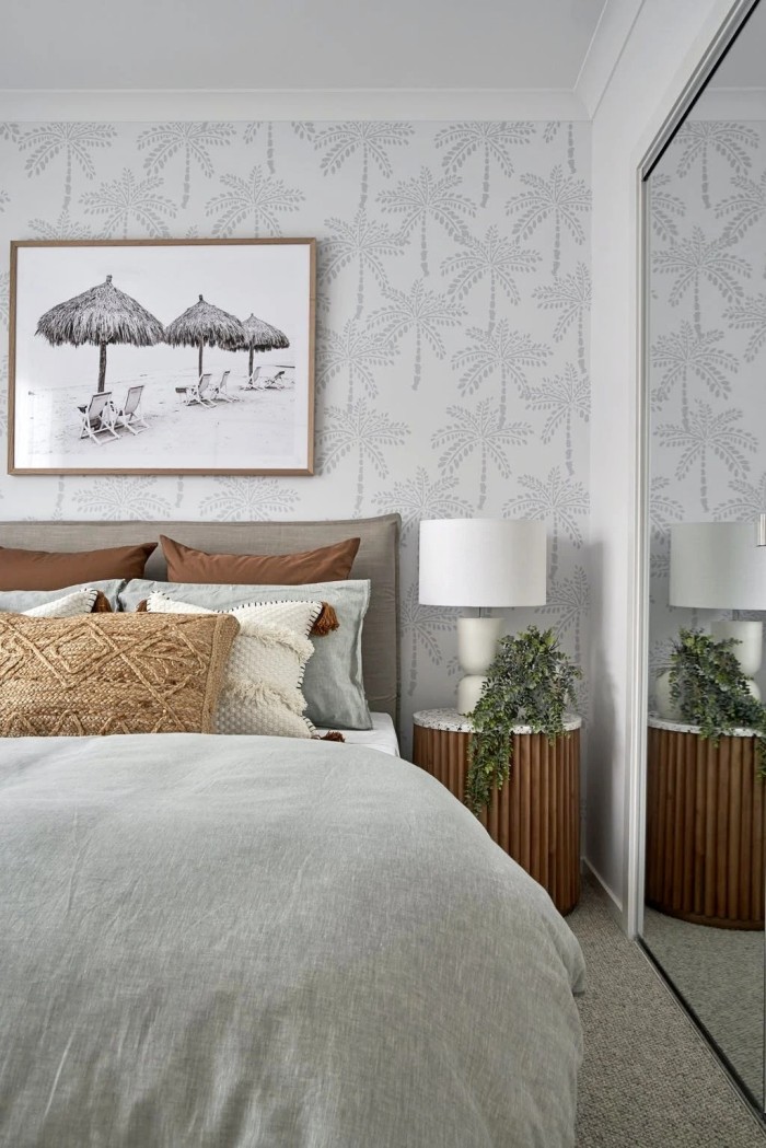 phòng ngủ ven biển với giấy dán tường cây cọ và tủ đầu giường bằng gỗ tròn với mặt trên bằng đá cẩm thạch